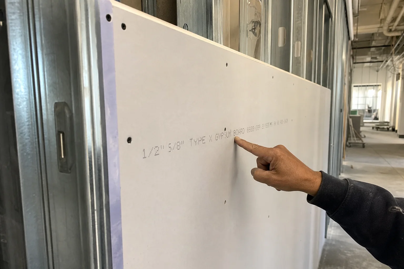 A contractor pointing to the printed Type X gypsum board label on a fire-rated drywall panel during a commercial tenant improvement in Chester County, PA