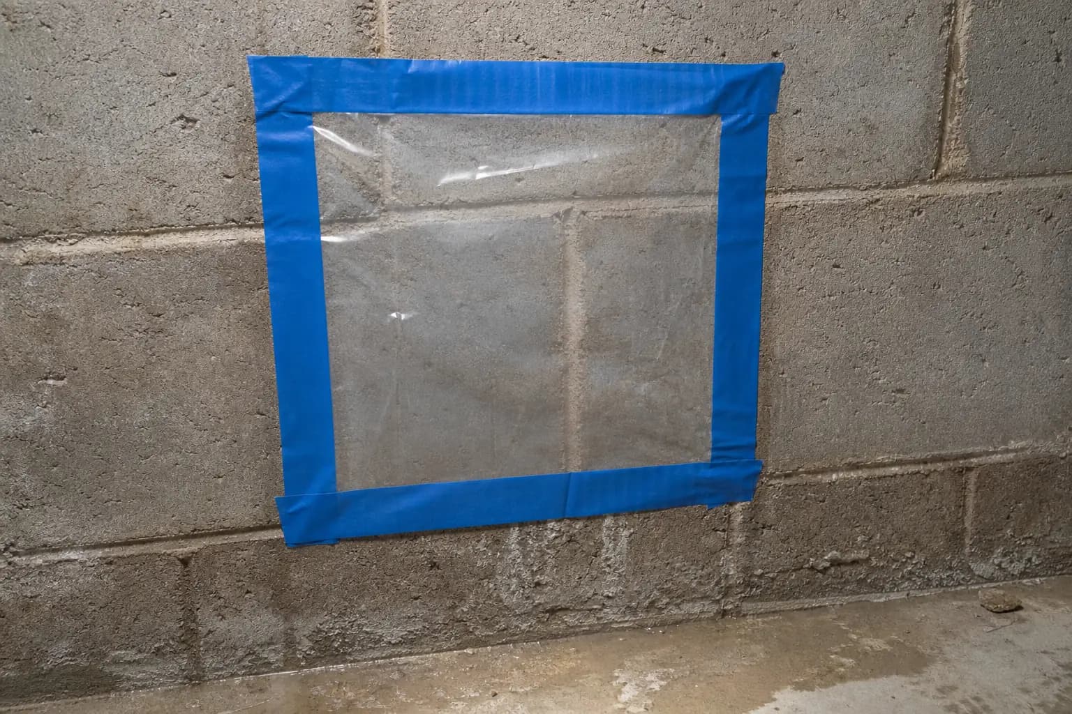 Clear plastic sheet taped to a concrete basement wall to test for moisture before basement finishing